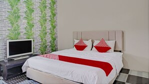 Habitación de hotel ordenada con una cama, un televisor sobre un mueble bajo y una pared de ladrillo con plantas verdes.