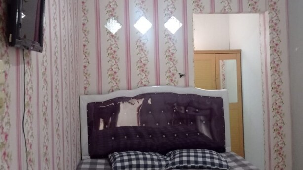 A bedroom with a bed, floral wallpaper, a mirror, and a television. - Hotel O Andesta Guest House SyariahNearAgrowisata Sungai Pinang Agro Nadin (Pekanbaru)