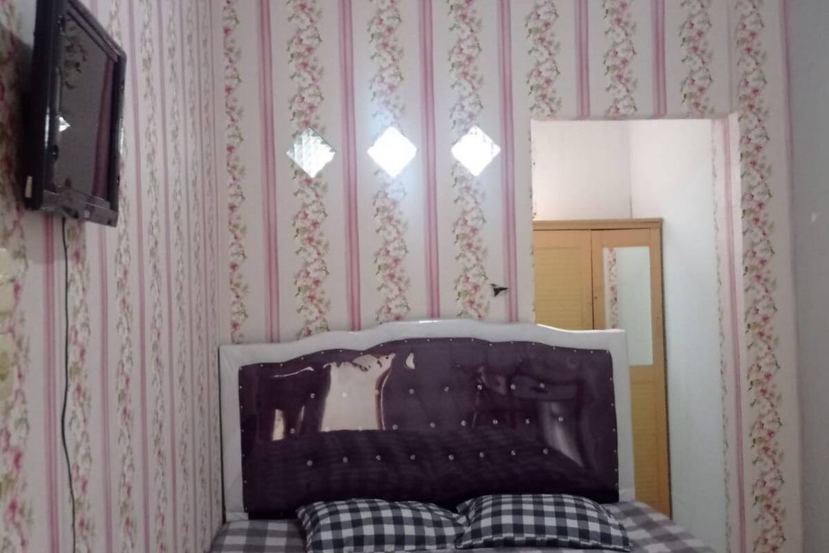 A bedroom with a bed, floral wallpaper, a mirror, and a television.