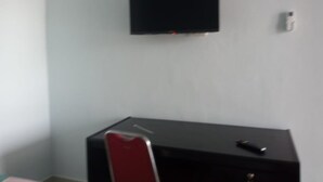A room with a flat-screen TV mounted on the wall, a black dresser with a red chair, and a small table with a remote control. - Hotel O Andesta Guest House SyariahNearAgrowisata Sungai Pinang Agro Nadin (Pekanbaru)