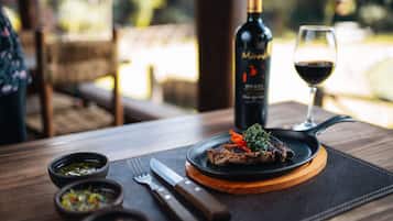 A dining table with a steak, a bottle of wine, and a glass of wine.