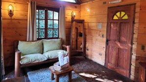 A cozy cabin interior with a wooden sofa, a small table, and a door with a unique window design. - Complejo Turístico Valle del Sol Quillón (Quillón)