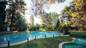 A swimming pool surrounded by grass and trees, with a fence and lounge chairs. - Complejo Turístico Valle del Sol Quillón (Quillón)