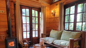 A cozy cabin interior with a wood-burning stove, a sofa with patterned cushions, and a rustic wooden table. - Complejo Turístico Valle del Sol Quillón (Quillón)