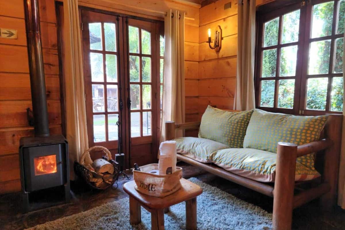 Ein gemütliches Blockhaussinnenzimmer mit Kaminofen, einer Couch mit gemusterten Kissen und einem rustikalen Holztisch.