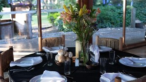 A dining table set for six with wicker chairs, a vase of flowers, and a view of greenery outside. - Complejo Turístico Valle del Sol Quillón (Quillón)