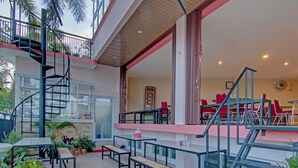An outdoor patio area with multiple tables and benches, a spiral staircase, and a view of the interior dining area with red chairs. - OYO 91951 Almira Homestay Syariah (Pekanbaru)