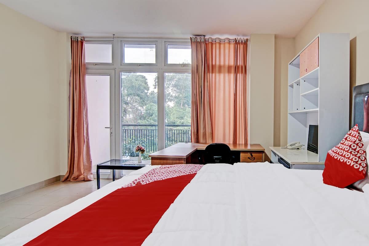 Habitación de hotel con cama, escritorio, silla, armario y ventana con cortinas.