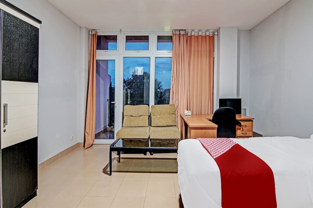 Habitación de hotel con cama, escritorio, silla y ventana con cortinas.
