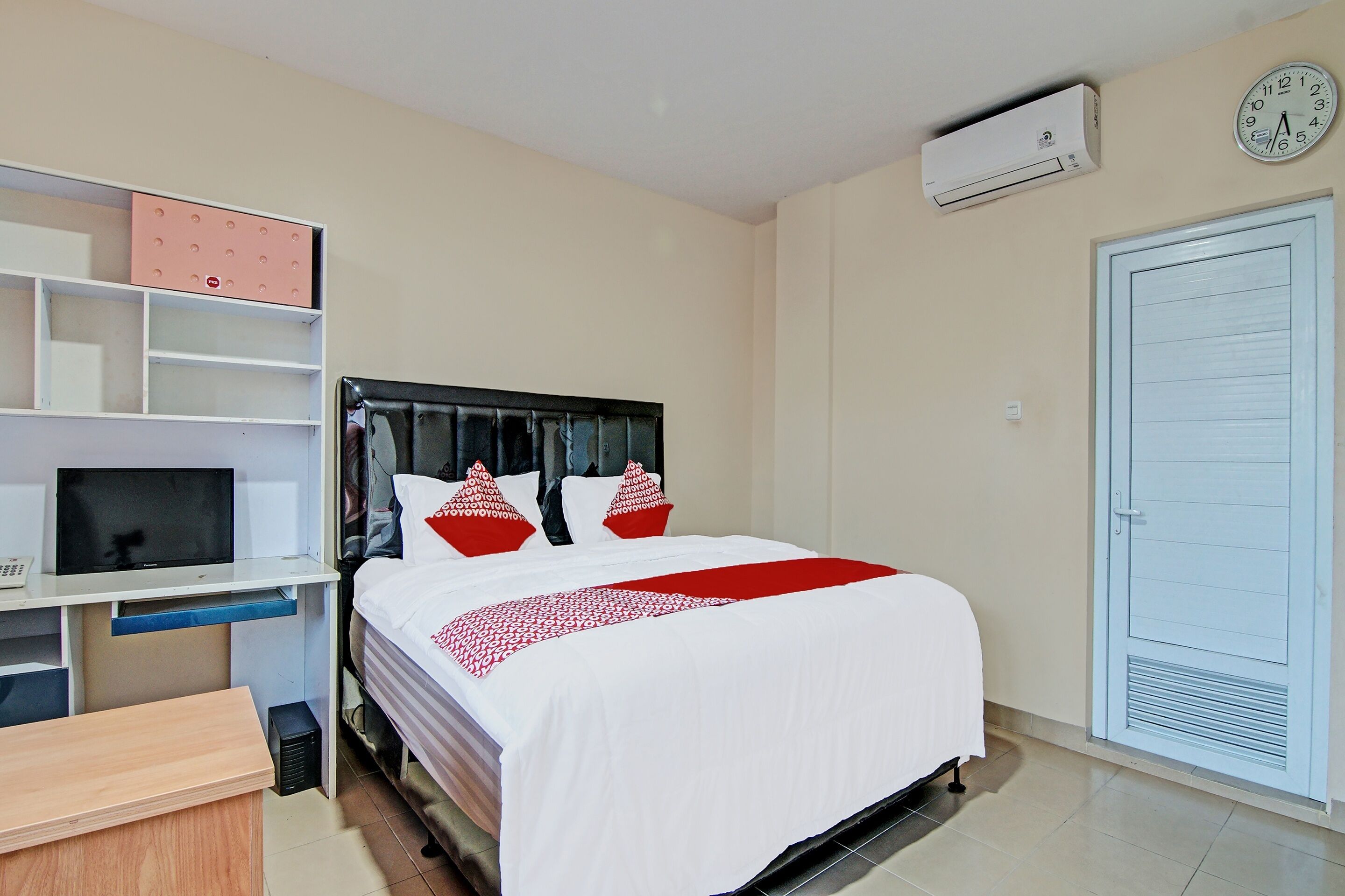 A hotel room with a bed, a desk with a computer, a TV, a wardrobe, and a door with a window.