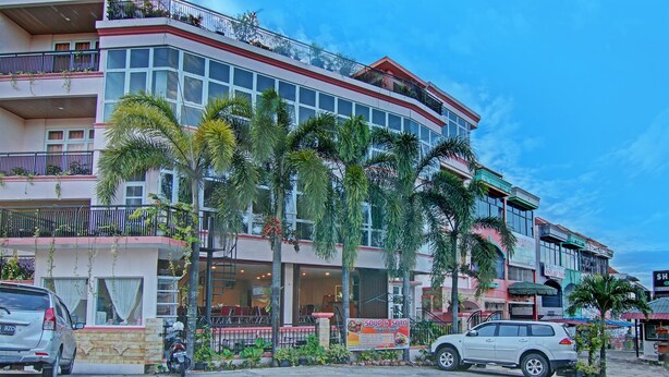 A multi-story building with balconies, a restaurant on the ground floor, and palm trees in front. - OYO 91951 Almira Homestay Syariah (Pekanbaru)