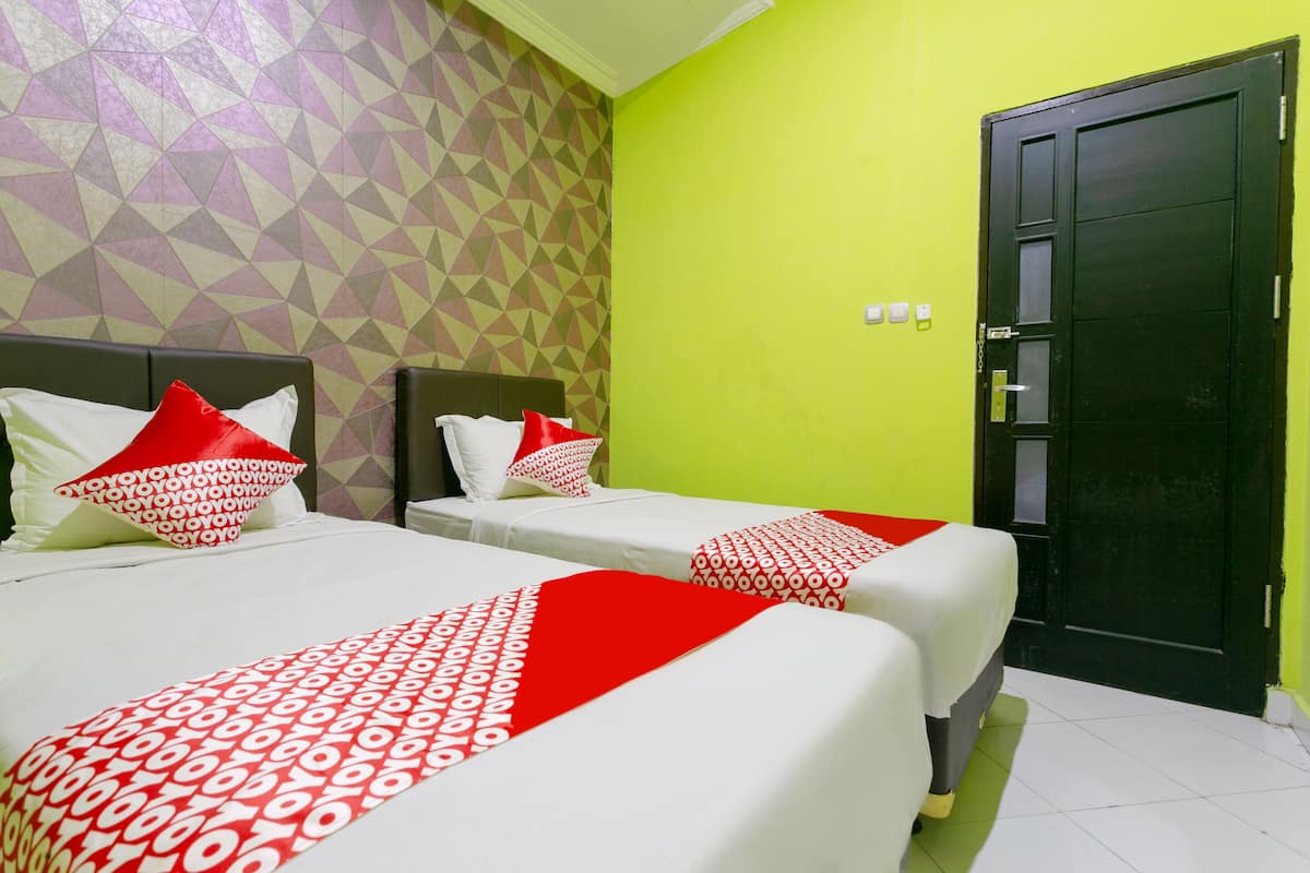 Une chambre d’hôtel avec deux lits, chacun agrémenté de draps rouges et blancs, un mur orné d’un motif géométrique et un mur vert.