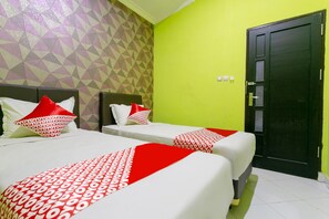 Habitación de hotel con dos camas, cada una con ropa de cama roja y blanca, un muro con estampado geométrico y una pared verde.