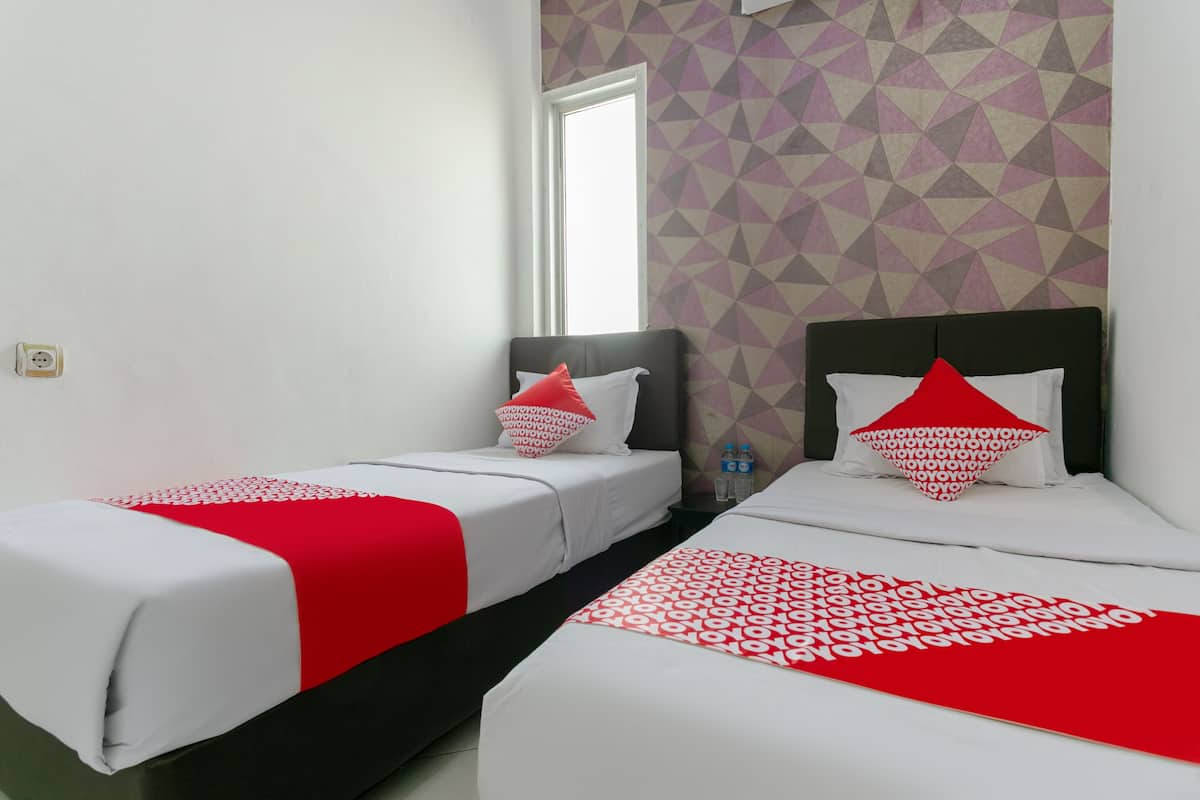 Une chambre d’hôtel avec deux lits, chacun recouvert d’une couvre-lit à motifs rouges et blancs, agrémenté d’oreillers blancs et d’un coussin décoratif rouge. La chambre est dotée d’un mur aux motifs géométriques et d’une fenêtre donnant sur l’extérieur.