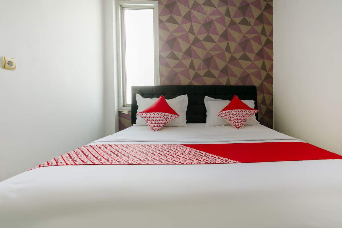 Un lit bien fait, avec une literie blanche et rouge, un mur orné d’un motif géométrique et une fenêtre laissant entrer la lumière naturelle.