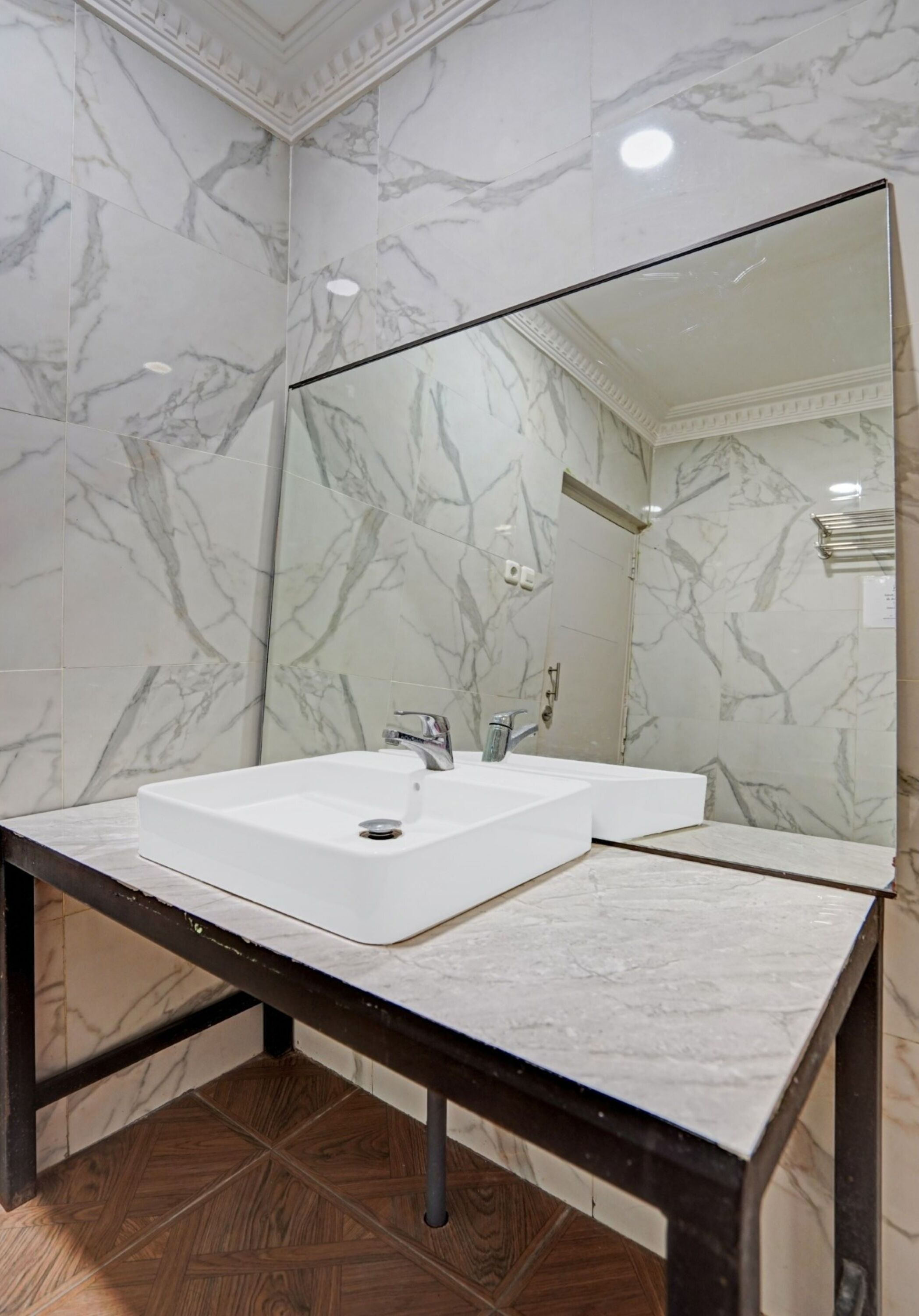 A bathroom with a white marble sink, a large mirror, and a wooden floor.