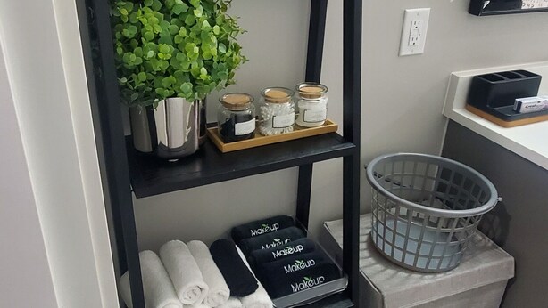 A black metal shelf with a sign reading 'Unwind,' holding a small plant, jars, and towels. - Cozy Suite: Private and peaceful 2 bedroom basement suite with keyless entry  (Edmonton)