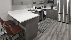 A modern kitchen with grey cabinets, stainless steel appliances, and a central island with bar stools. - Cozy Suite: Private and peaceful 2 bedroom basement suite with keyless entry  (Edmonton)