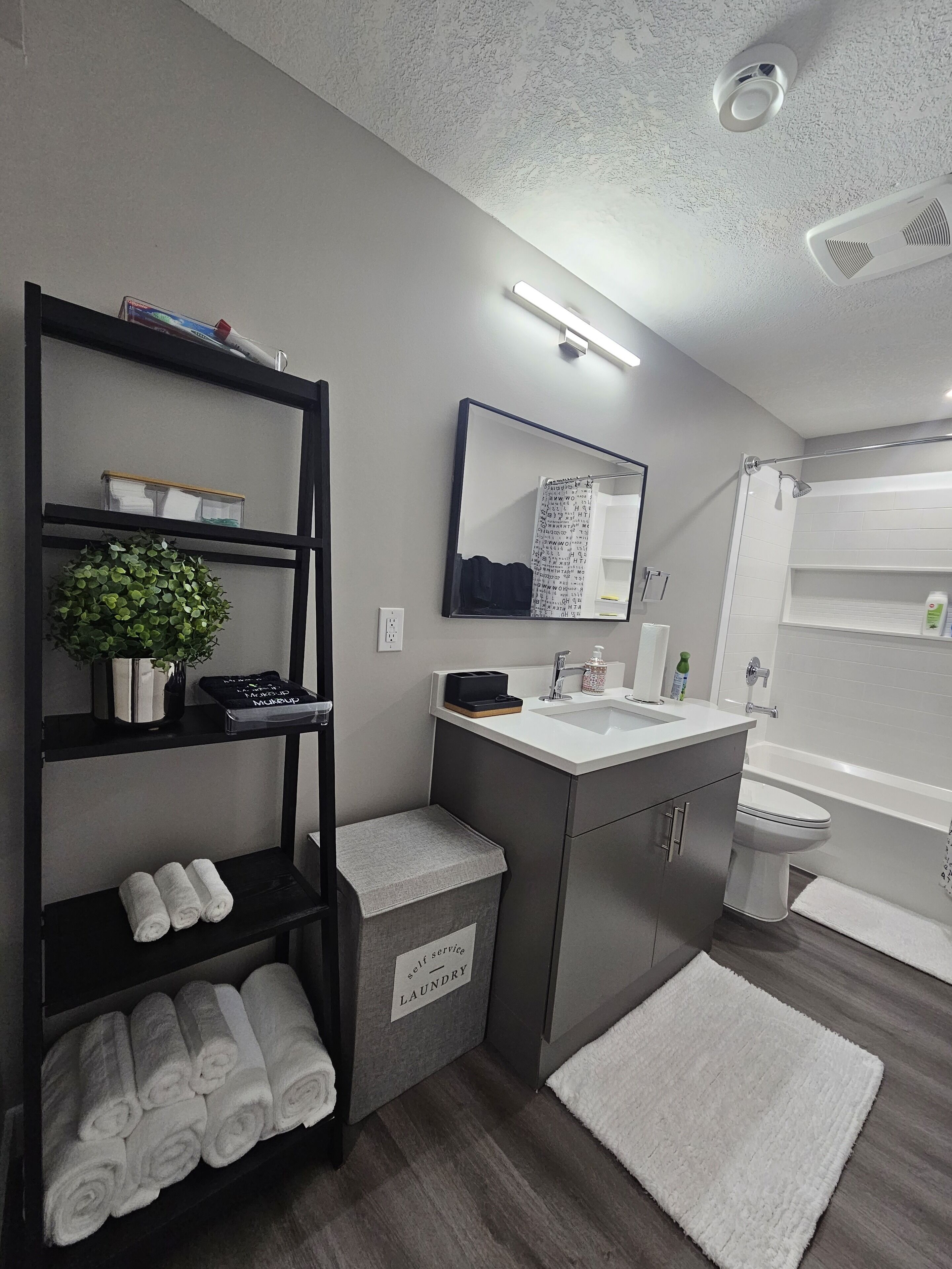 Een moderne badkamer met een douche, toilet en wastafel. Er is een plank met handdoeken en een potplant.