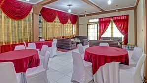 A banquet hall with round tables covered in red tablecloths, white chairs, and red drapes on the windows. - OYO Life 91480 Putridapisa Syariah (Sumedang)