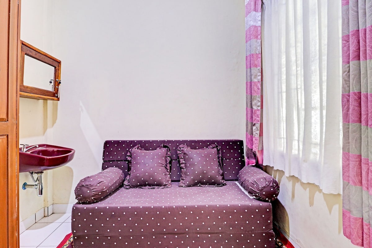 A small, cozy room with a single bed, a bedside table, a mirror, and a window with curtains.