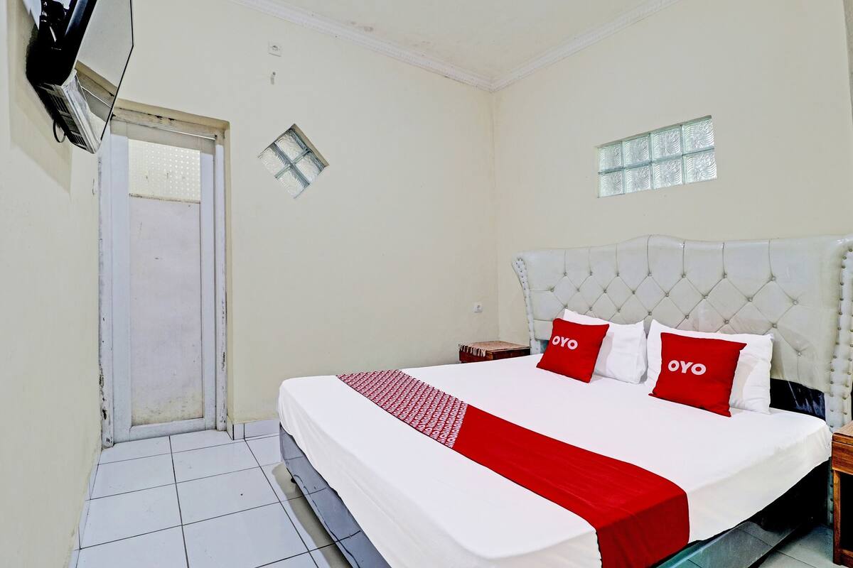 A hotel room with a large bed, a small bedside table, a window, and a door.