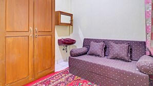 A room with a wooden wardrobe, a purple sofa with polka dots, a red sink, and a patterned rug. - OYO Life 91480 Putridapisa Syariah (Sumedang)