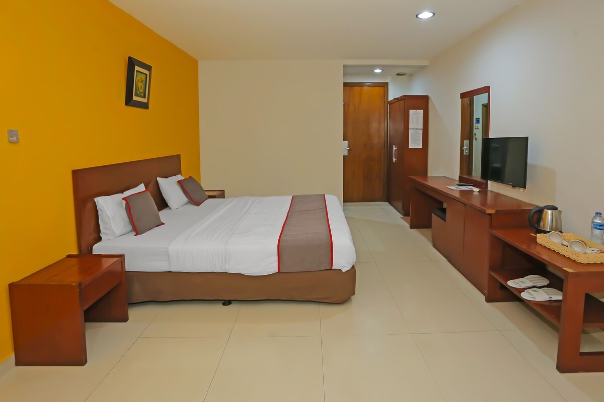A hotel room with a bed, bedside table, TV, and a wooden dresser.