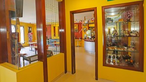 A hotel lobby with a yellow wall, a reception desk, and a glass display case with souvenirs. - Townhouse OAK Hotel Fiducia Pasar Minggu (Jakarta)