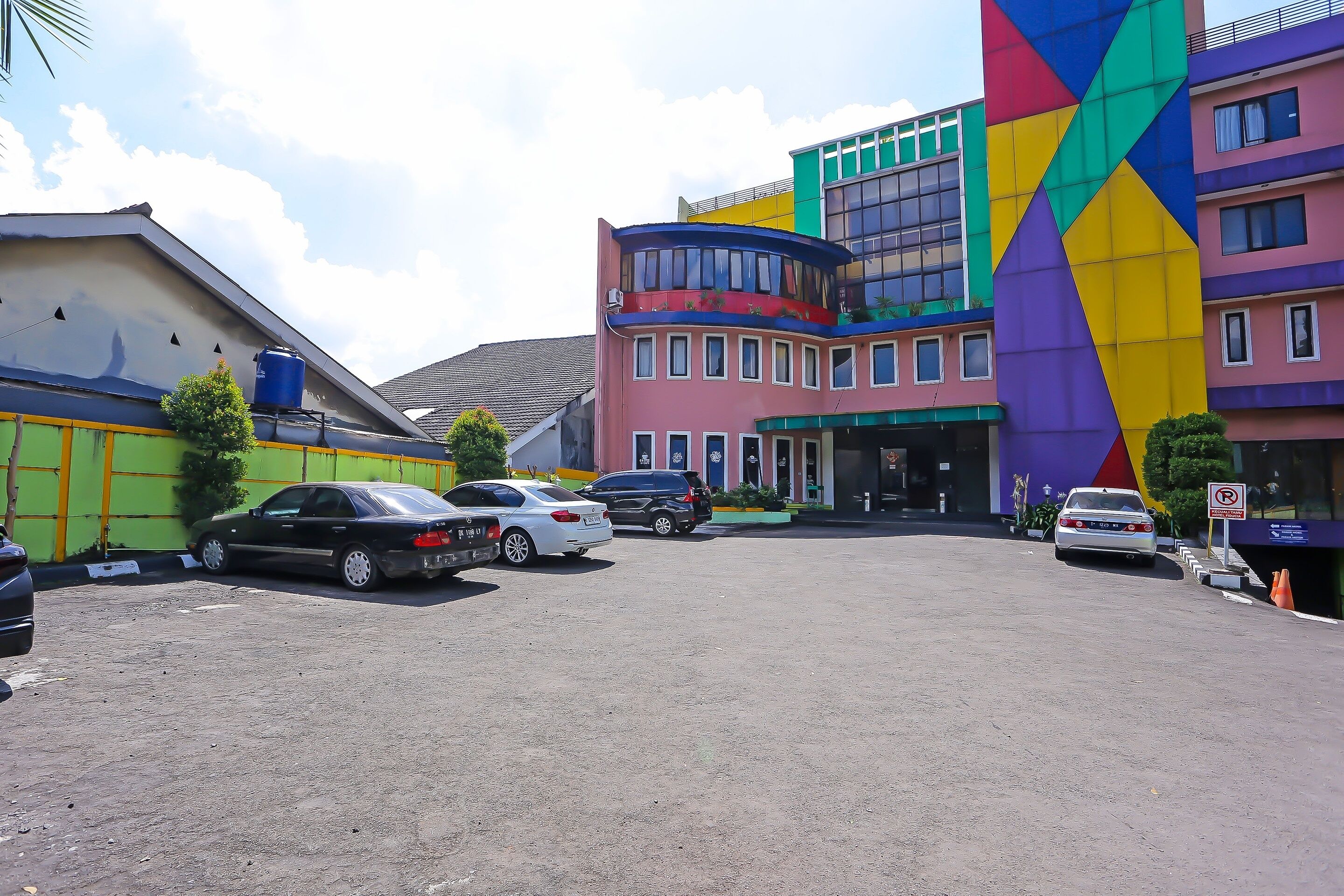 A parking lot with several cars, a building with colorful facades, and a large water tank on the roof.