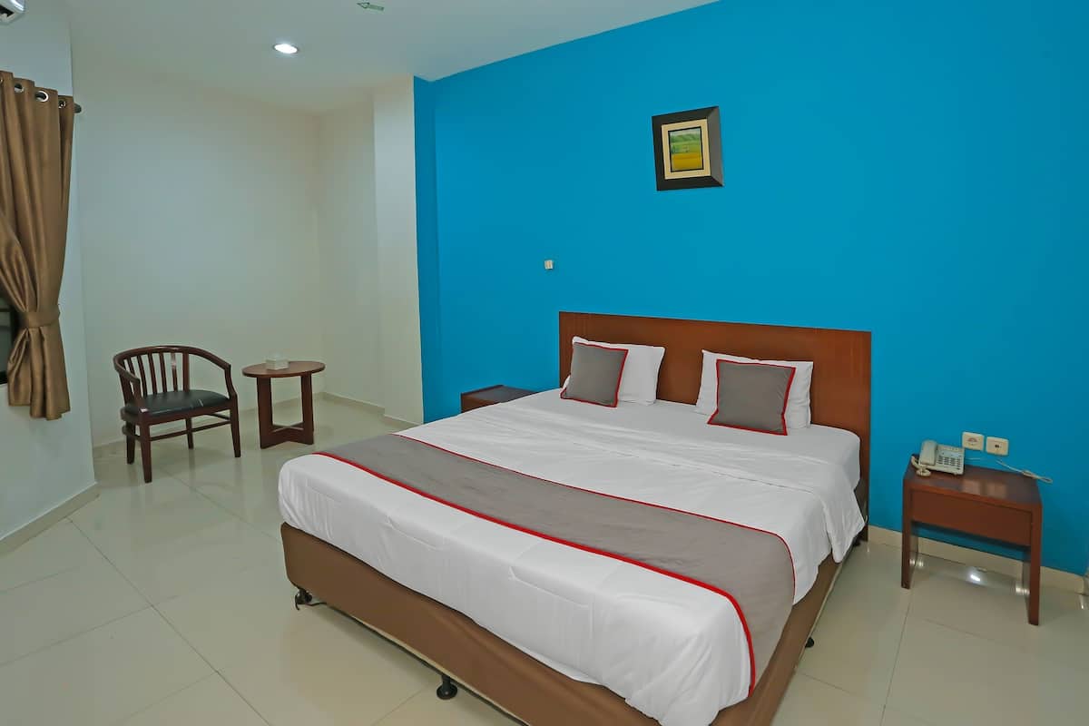 Une chambre d’hôtel avec un grand lit, une chaise, une petite table et une table de chevet avec un téléphone.