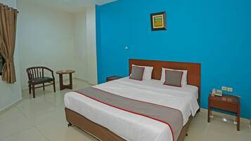 A hotel room with a large bed, a chair, a small table, and a nightstand with a phone.