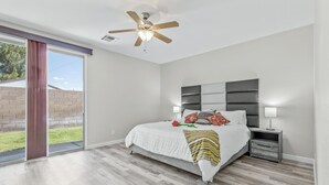 Une chambre avec un grand lit, un ventilateur de plafond, une table de chevet et une porte-fenêtre coulissante donnant sur l’extérieur.