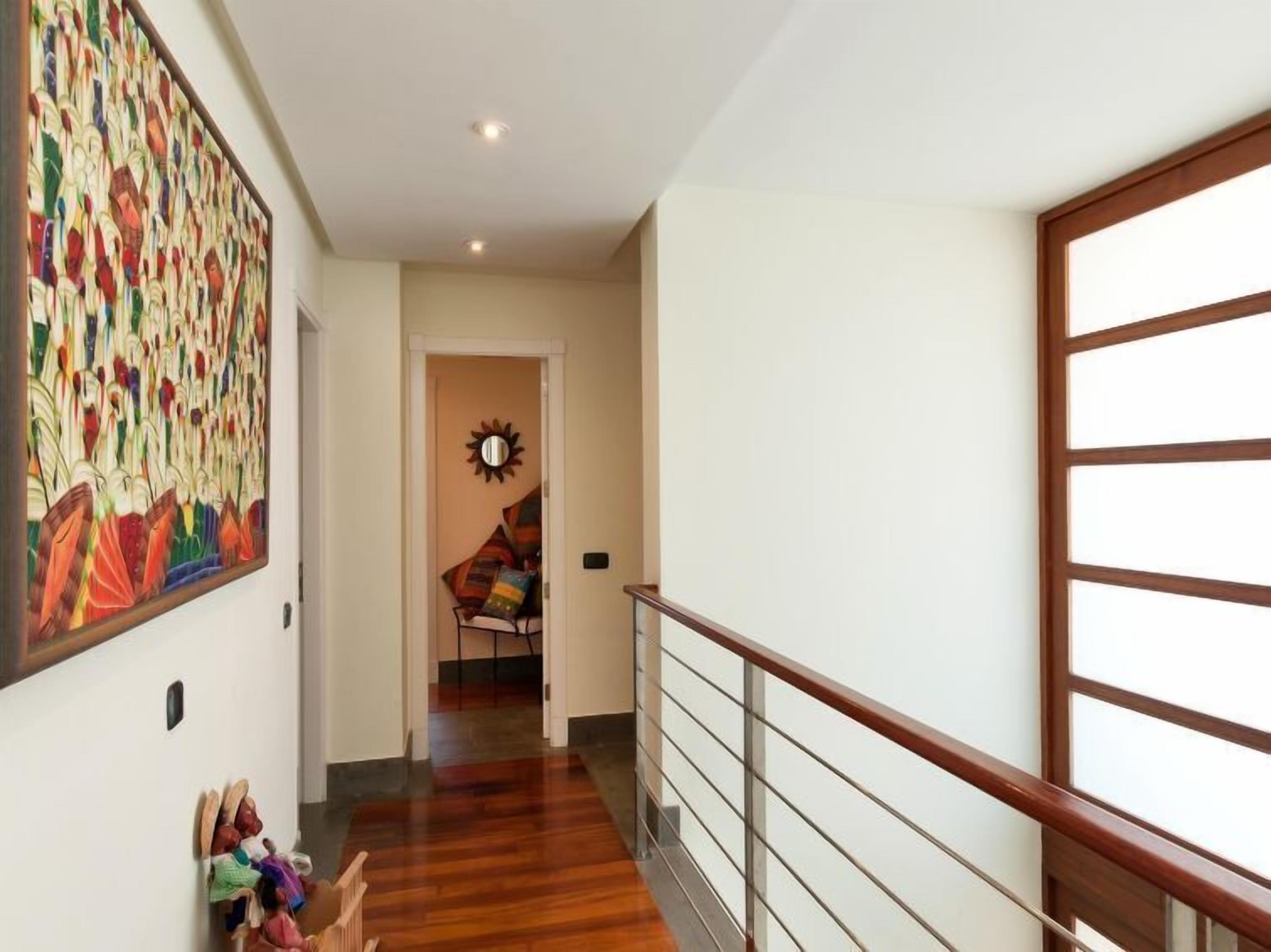 Un couloir doté d’un plancher en bois, une grande peinture abstraite sur le mur de gauche et un miroir en forme de soleil accroché au mur.