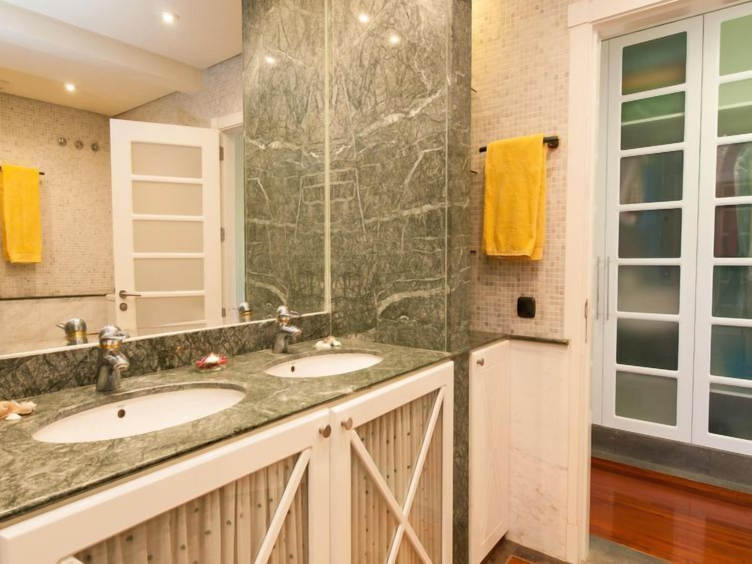 Une salle de bain avec deux lavabos, un miroir et une porte donnant sur une pièce.