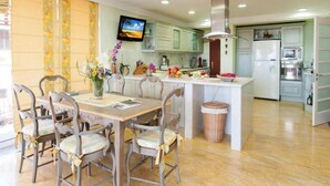 Cozinha moderna com armários brancos, uma ilha central e um espaço de refeições com cadeiras e uma mesa.
