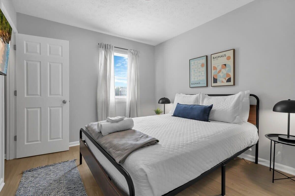 A neatly arranged bedroom with a bed, a bedside table, a lamp, and a window with curtains.