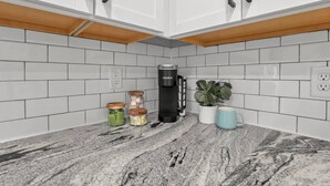 A kitchen with white cabinets, a coffee maker, jars, a plant, and a mug. - Urban Townhouse Near Downtown | 2BR + W/D (Columbus)