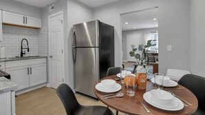 A modern kitchen with white cabinets, a stainless steel refrigerator, and a dining area with a wooden table set for two. - Urban Townhouse Near Downtown | 2BR + W/D (Columbus)