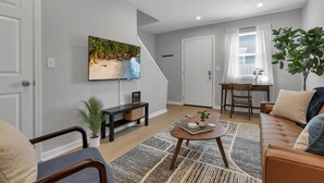 A living room with a television, a sofa, a coffee table, and a plant. - Urban Townhouse Near Downtown | 2BR + W/D (Columbus)