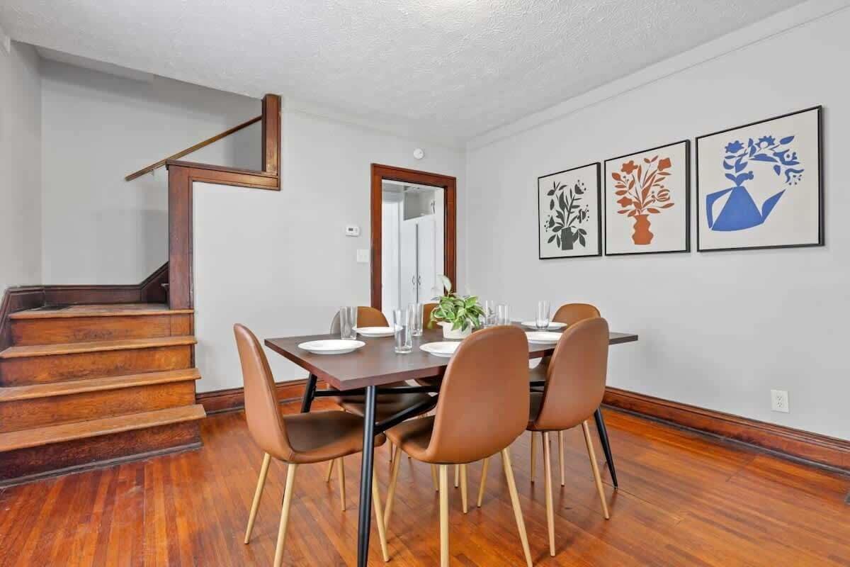 A dining area with a wooden staircase, a dining table set for four, and three framed artworks on the wall.