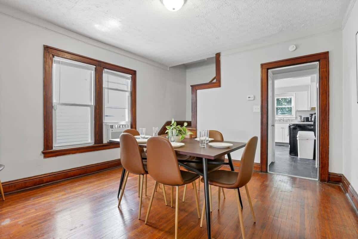 A dining area with a wooden table and chairs, a plant on the table, and a view into the kitchen through an open doorway.