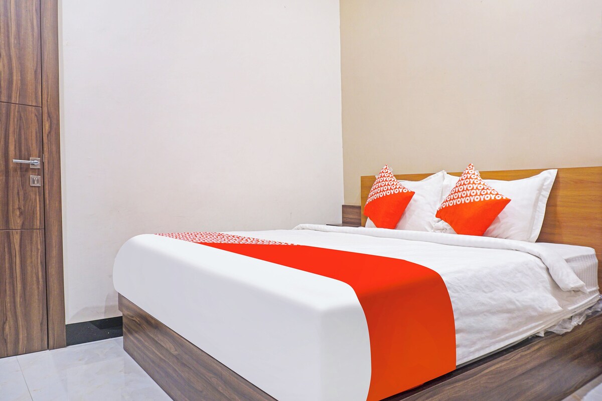 Cama bem arrumada com roupa de cama branca e laranja, cabeceira de madeira e uma porta à esquerda.