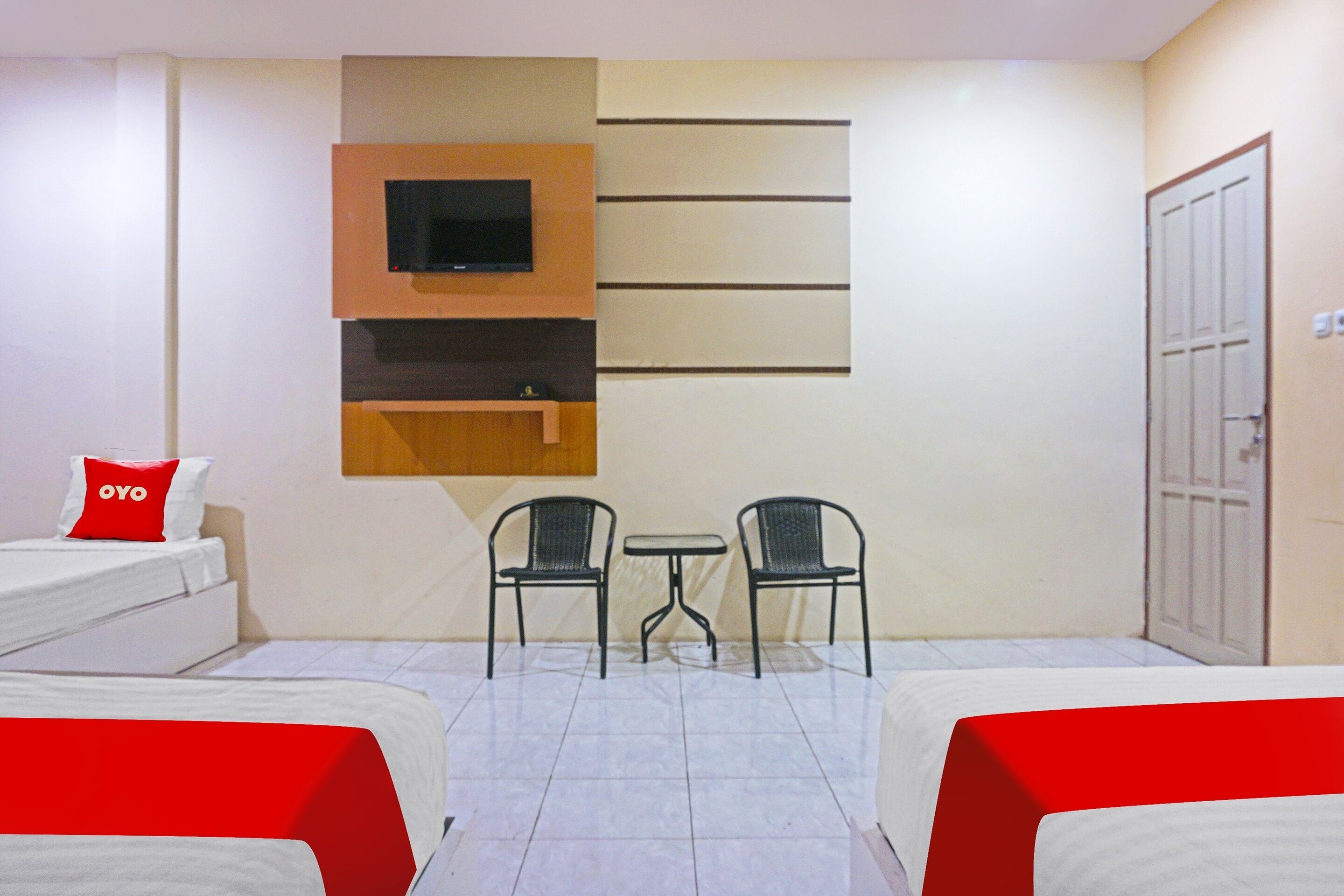 Habitació d'hotel amb dos llits, un televisor fixat a la paret, una taula petita amb cadires i una porta.