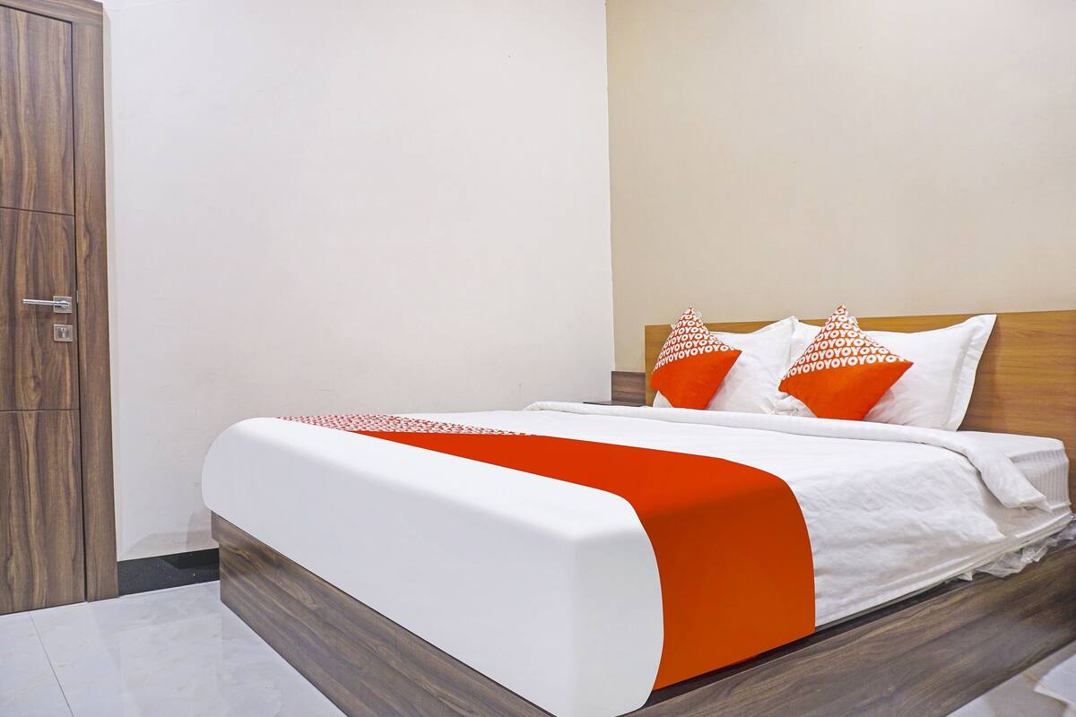 Un lit bien fait, avec une literie blanche et orange, une tête de lit en bois et un mur sobre.