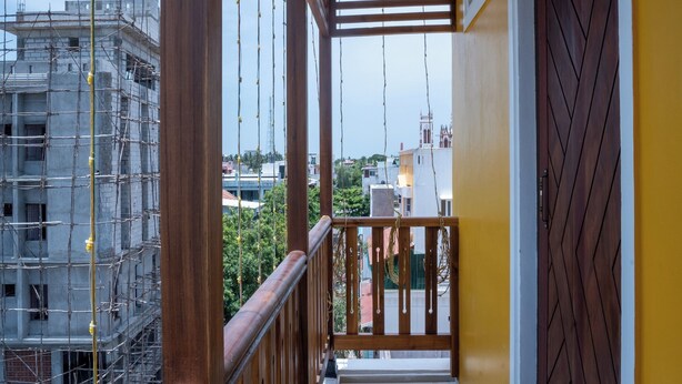 A balcony with a wooden railing, a view of a building under construction, and a yellow wall with a decorative door. - Le Suresh Residency (Puducherry)