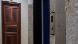 A wooden door with a number plate, a marble wall, and an elevator with a control panel. - Le Suresh Residency (Puducherry)