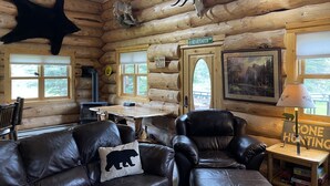 A log cabin interior with a fireplace, leather sofas, a hunting-themed lamp, and a bear-shaped pillow. - Tweek's Cabin- luxury cabin with yard, fire pit, and hot tub!!!

 (Cody)