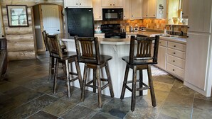 A log cabin kitchen with a central island, bar stools, a refrigerator, microwave, stove, and wooden cabinets. - Tweek's Cabin- luxury cabin with yard, fire pit, and hot tub!!!

 (Cody)