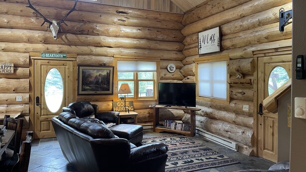 A log cabin interior with a leather sofa, a television, and a mounted deer skull. - Tweek's Cabin- luxury cabin with yard, fire pit, and hot tub!!!

 (Cody)